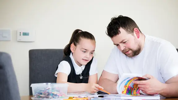 Man And Daughter Sit At A Table Doing Homework Together